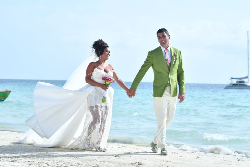 Bride and groom on a beach, with the groom wearing a green tailored jacket
