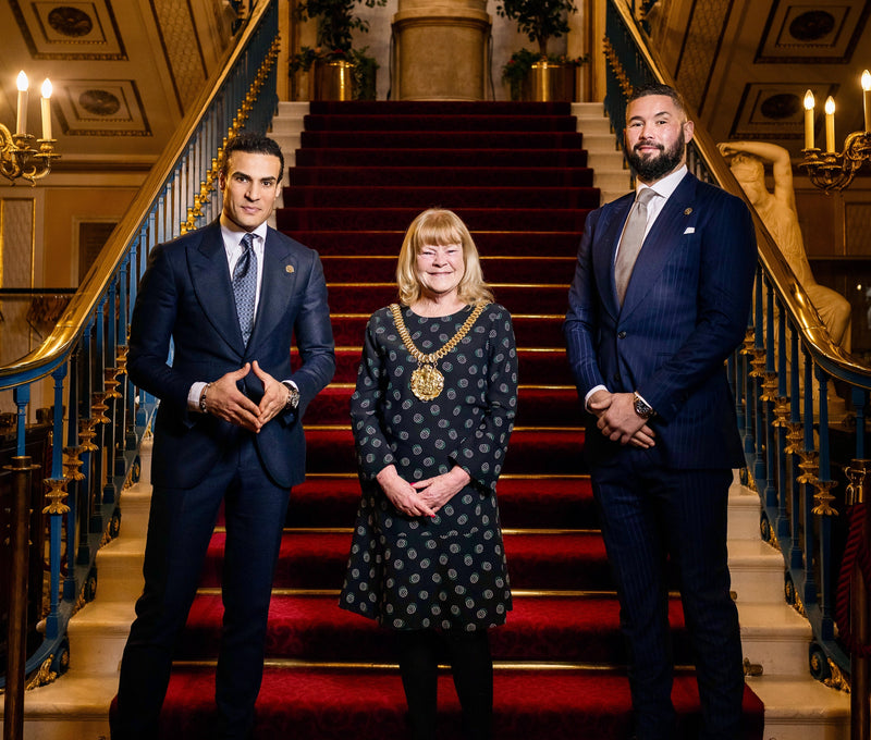 Two men in Signature Bespoke tailoring with a civic guest on a grand staircase