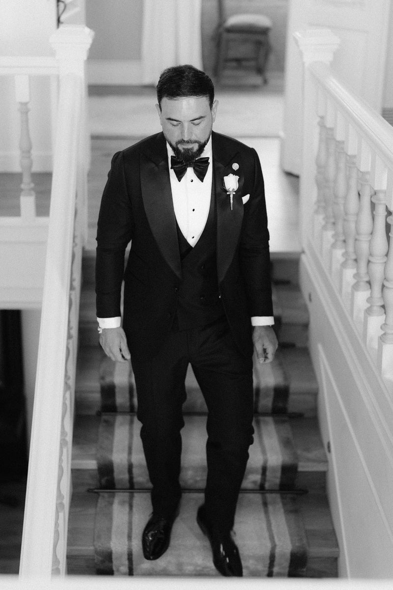 Groom wearing a black dinner suit and bow tie on a staircase