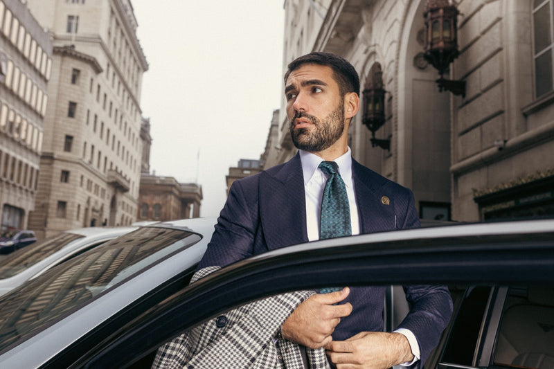 Man in a navy bespoke suit beside a car on a city street