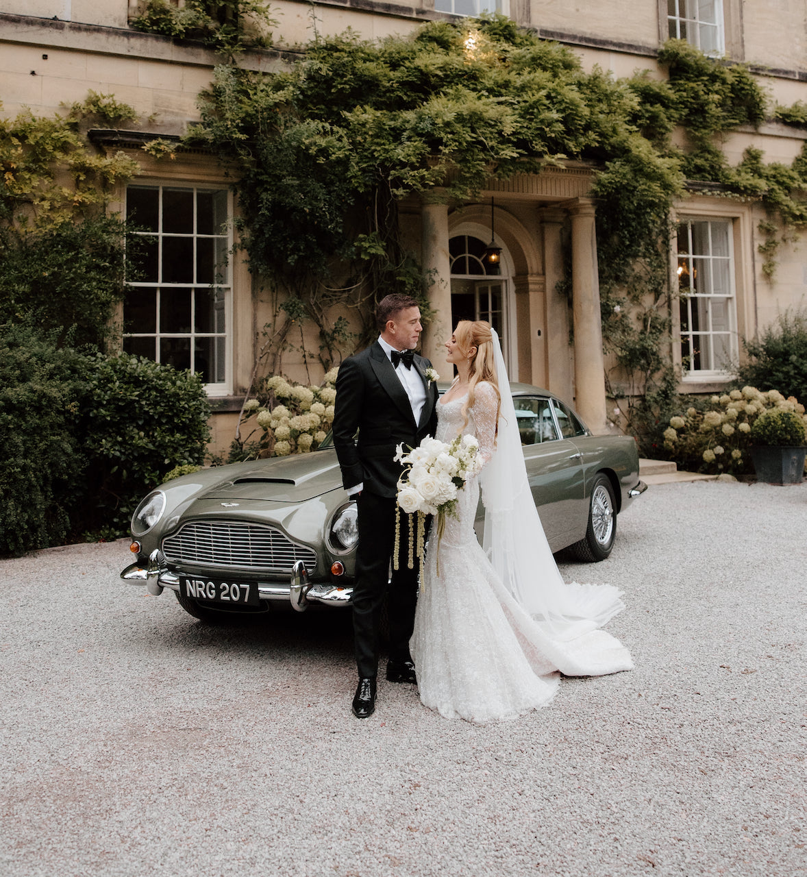 Bride and groom beside a classic Aston Martin outside a country house