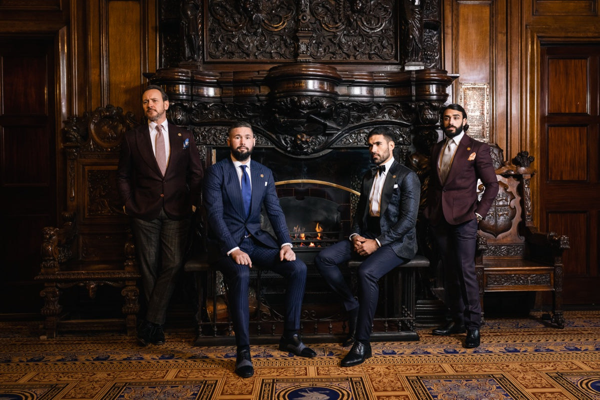 Four men in tailored suits and eveningwear posed by an ornate fireplace